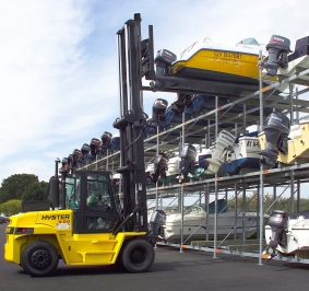 Chariot élévateur déposant un bateau sur le dernier niveau d’un rack de stockage extérieur
			