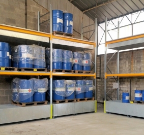 Zware rekken met opvangbakken voor vaten met chemische producten in een hangar
			